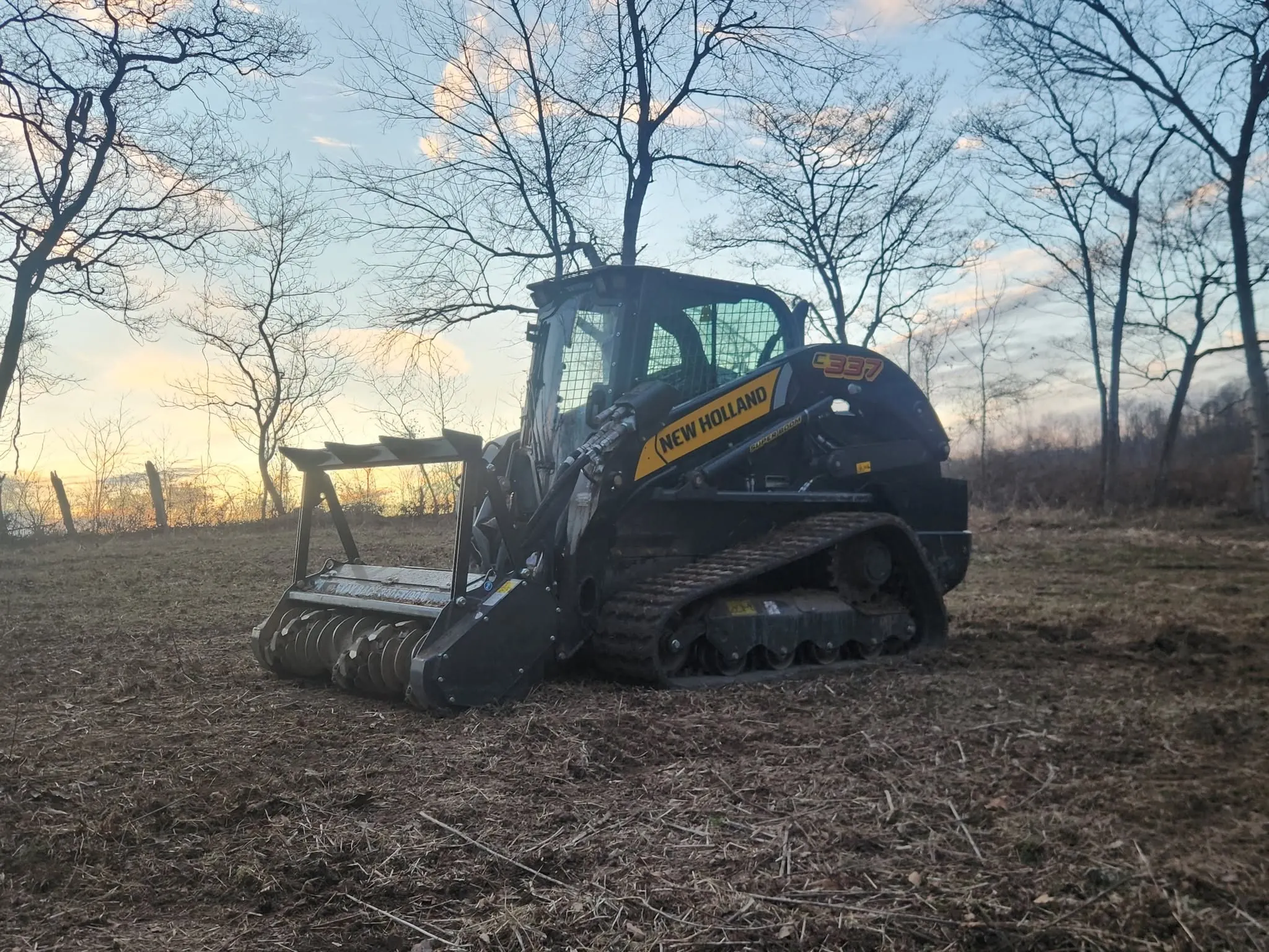 BlueGrid's New Holland C337 track loader with its mulching head, working at dusk